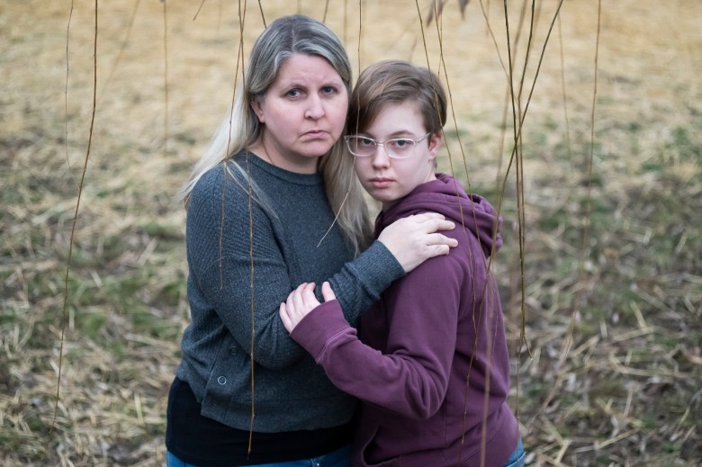 Lisa Norris stands hugging her daughter Hannah. Lisa has long blond hair and is wearing a blue sweater. Hanna has short brown hair and wears glasses and a purple hoodie.