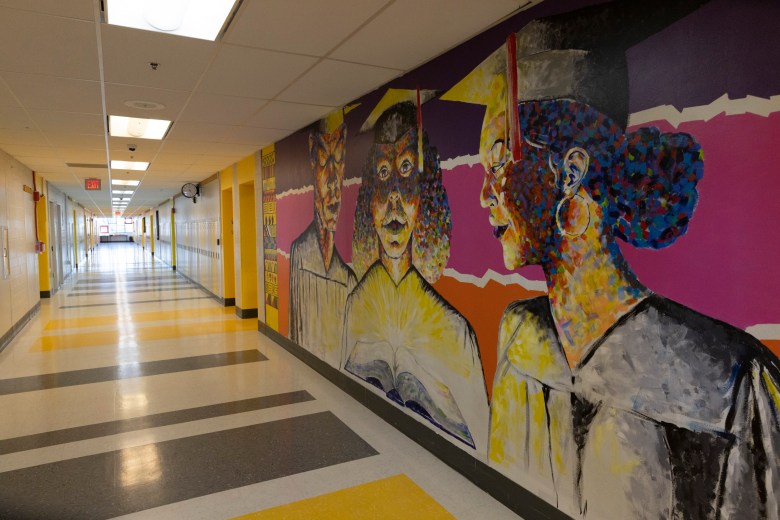 An empty school hallway. One wall is decorated by a painted mural of people in graduation caps and gowns.