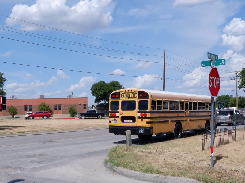A school bus drives past the Travis Elementary school with the Texas flag in the background.