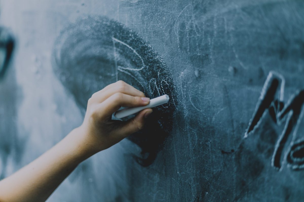 A young person's hand writes on a chalkboard.