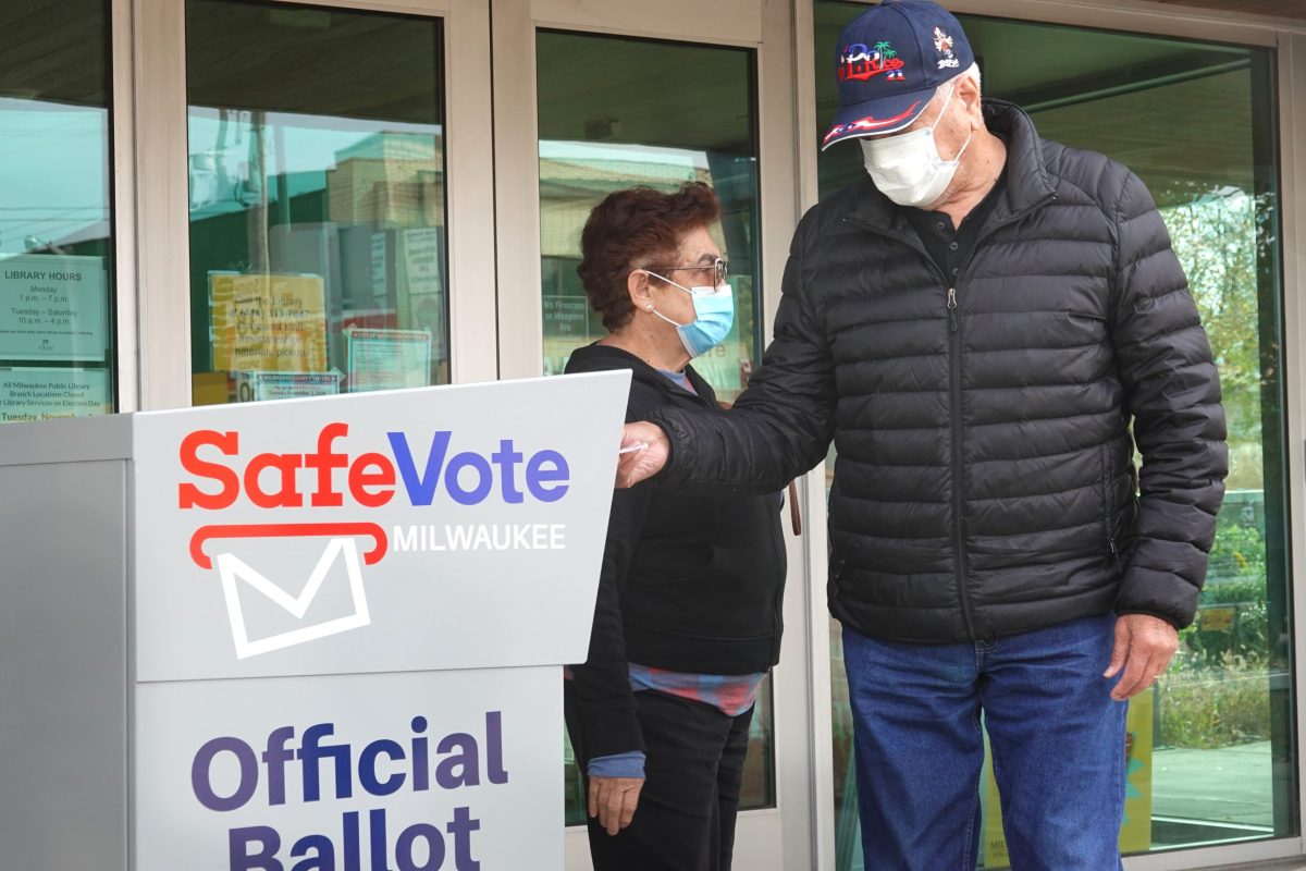 A voter wearing a mask puts a ballot into an election drop box.
