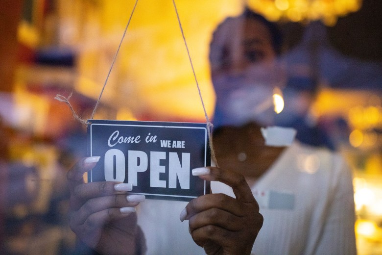 Woman turning an open sign on glass front door of coffee shop.