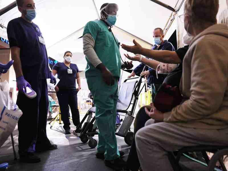 Clinicians evaluate an incoming patient with his arms raised in a triage tent set up in the parking lot at Providence St. Mary Medical Center amid a surge in COVID-19 patients.