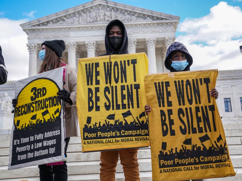A woman and two boys, all wearing face masks to protect against COVID-19, stand outside the U.S. Supreme Court with signs. Her sign reads: "3rd Reconstruction: It's time to fully address poverty & low wages from the bottom up!" The boys' signs both read: "We won't be silent: Poor  People's Campaign. A national call for moral revival."