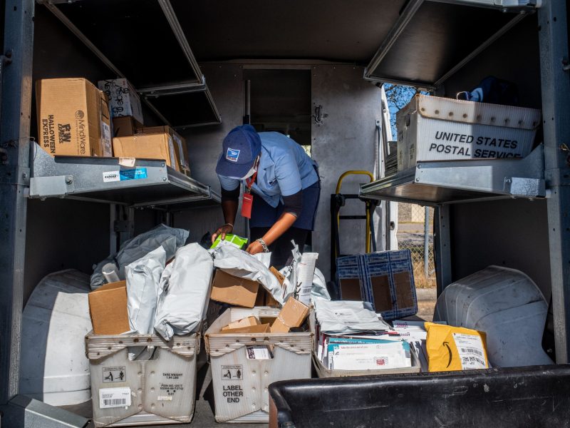 A mail carrier sorts through mail in the back on a postal vehicle.