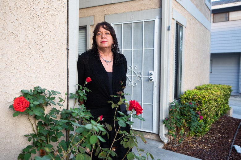Beth Petersen, dressed in all black, stands by a rose bush as she looks toward the camera. 