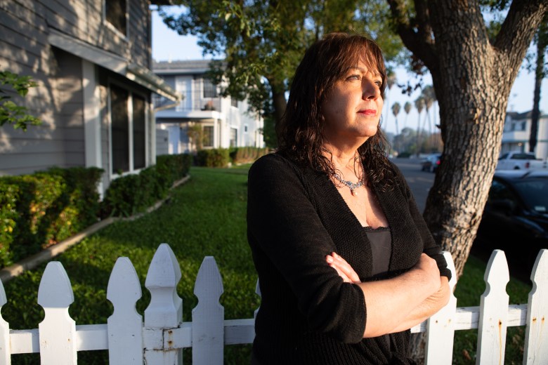 Beth Petersen, dressed in all black, stands next to the picket fence out side of her apartment.