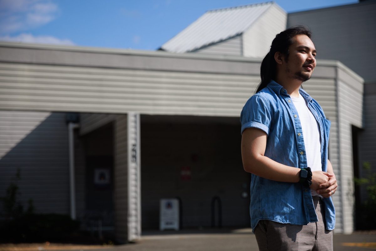 MJ Dizon stands outside the North Thurston Public Schools' Family & Youth Resource Center in a blue button down shirt. Dizon has long black hair and is smiling.